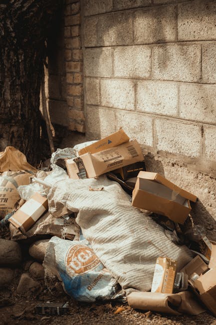 Three large black plastic garbage bags filled with waste are placed on a sidewalk in front of a black metal fence with vertical bars. The bags appear to contain household or garden waste, and are arra